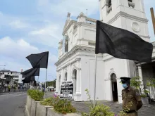 A policeman stands guard at St. Anthony's church in Colombo, Aug. 21, 2021, next to a placard and black flags placed in protest for the alleged failure to prosecute those responsible for the bomb attacks of Easter Sunday 2019. Credit: Ishara S. Kodikara/AFP via Getty Images.